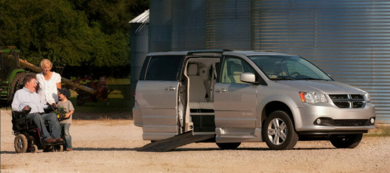 Image of a man with his wife and child outside their silver BraunAbility Dodge Grand Caravan wheelchair van at their farm
