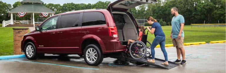 Family pushing daughter in wheelchair up ramp of rear entry wheelchair van at a park