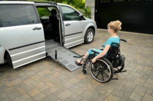 silver minivan in driveway with lady in blue dress sitting in manual wheelchair being pulled up her ramp using power-pull device from adapt solutions