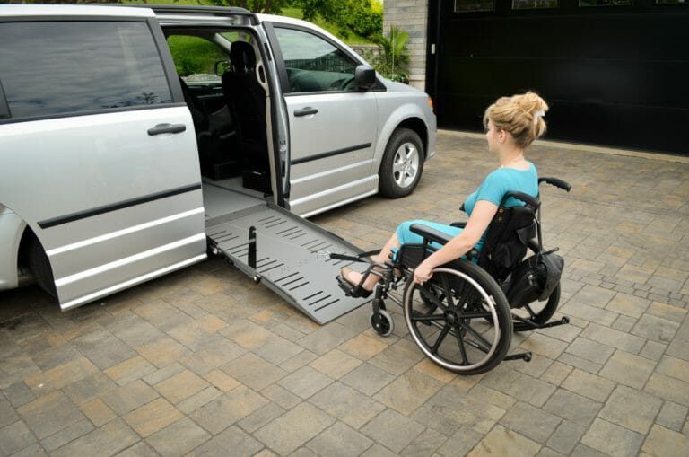 silver minivan in driveway with lady in blue dress sitting in manual wheelchair being pulled up her ramp using power-pull device from adapt solutions