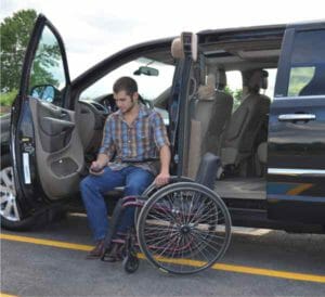 Man unloading his manual wheelchair from a black minivan using his Hi-lift from adapt solutions
