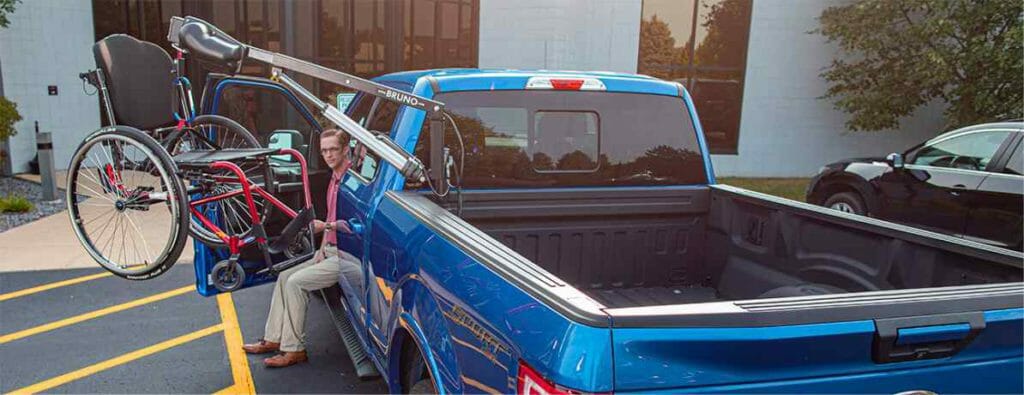 Man sitting in seat of blue pickup truck operating his Bruno Out-Sider wheelchair lift