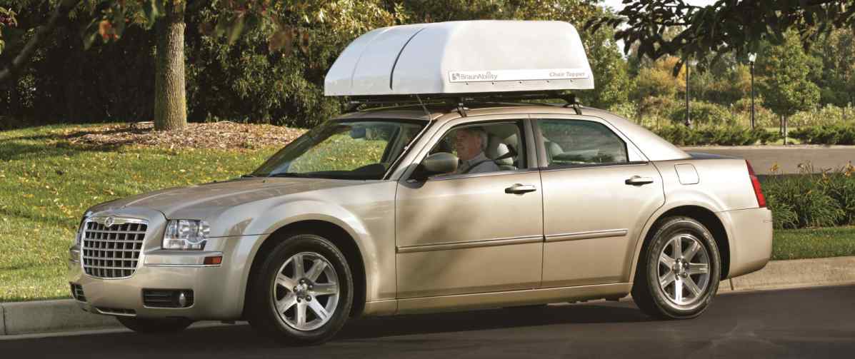 gold car with man driving down road with a BraunAbility Chair Topper manual wheelchair carrier installed on roof