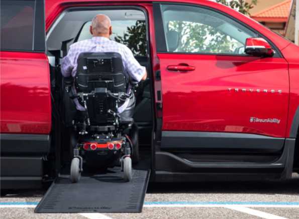 Closeup of red Chevrolet Traverse wheelchair SUV from BraunAbility with a man in a power wheelchair going up ramp
