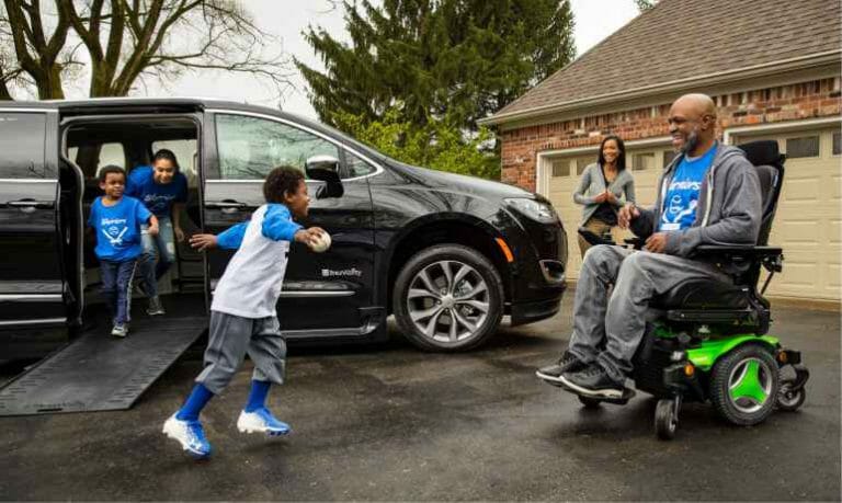 Grandfather in his driveway in wheelchair with grandkids playing around his wheelchair van
