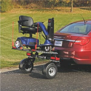 Blue mobility scooter on a Bruno Chariot wheelchair lift & mobility scooter carrier that is being towed behind a red car