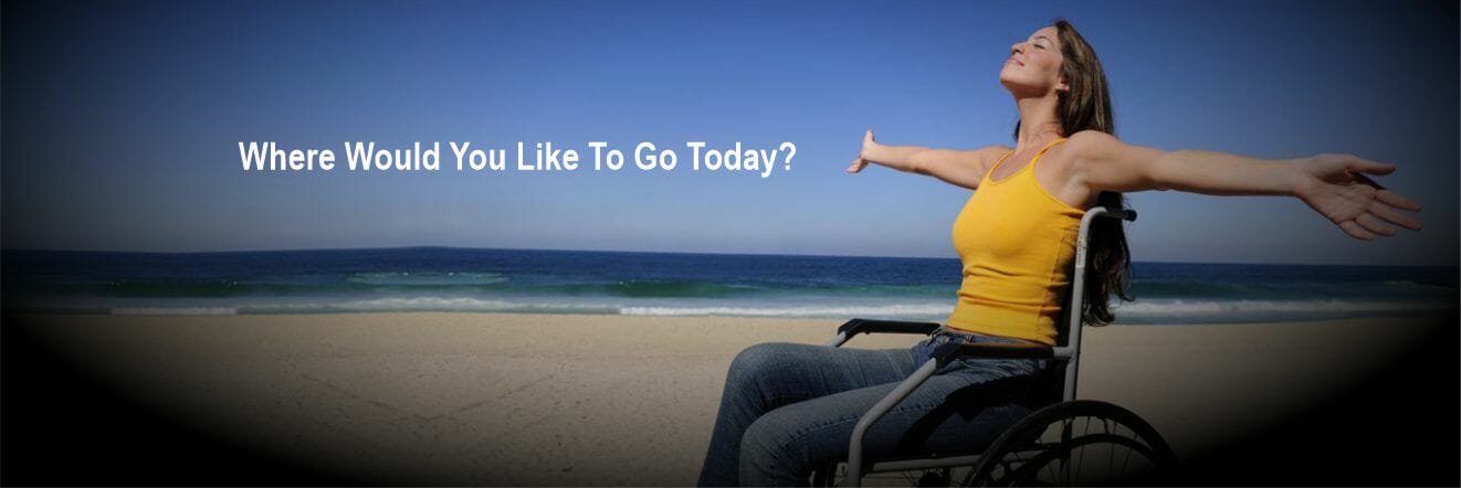 Women in yellow shirt sitting in wheelchair with arms out wide on the beach
