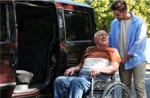 Young man pushing older man in wheelchair to enter a van